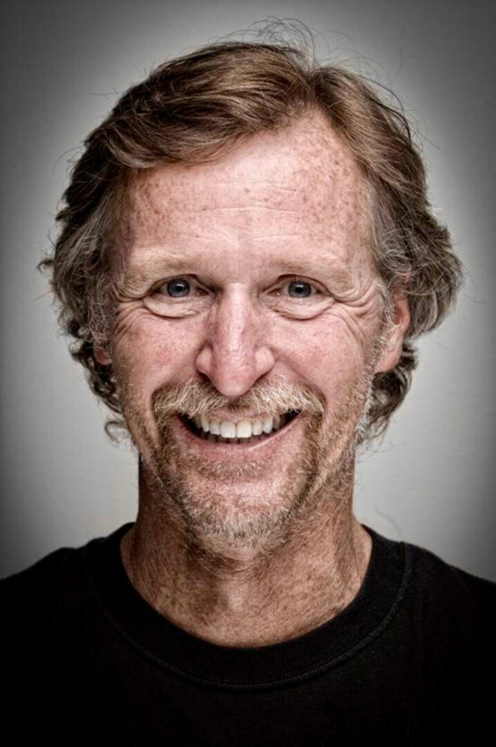 Author Tony McLean Brown Happy Guide A man with long hair and a beard smiling.