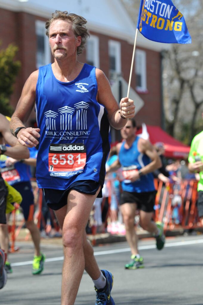 Tony McLean Brown Boston Strong A man running in the marathon while holding onto a stick.