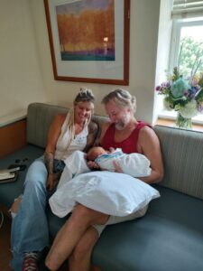 june bug kid tmb Two women sitting on a couch with a baby.