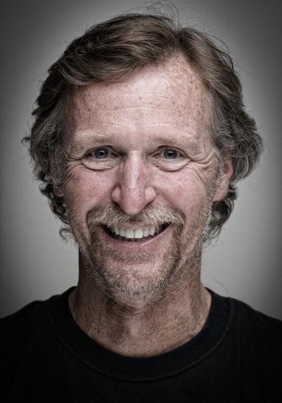 A man with long hair and a beard smiling.